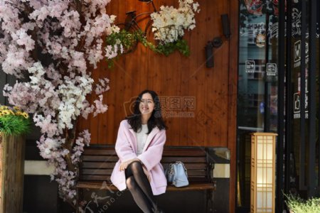 女性在粉红色的外套坐在布朗板凳近樱花