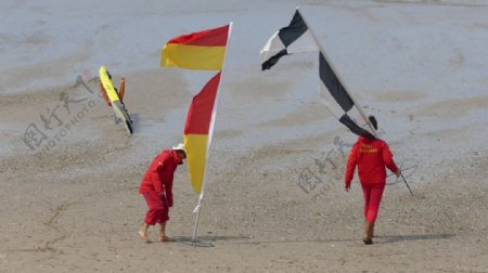 手拿旗帜的两人走在沙滩上