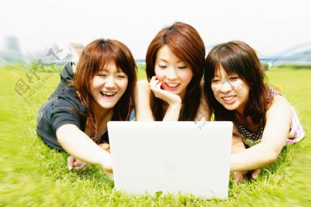 草地上开心玩电脑的三个美女图片