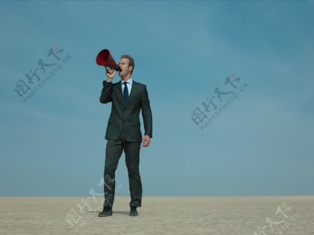 拿着扩音器在沙漠中呐喊的外国商业男人图片